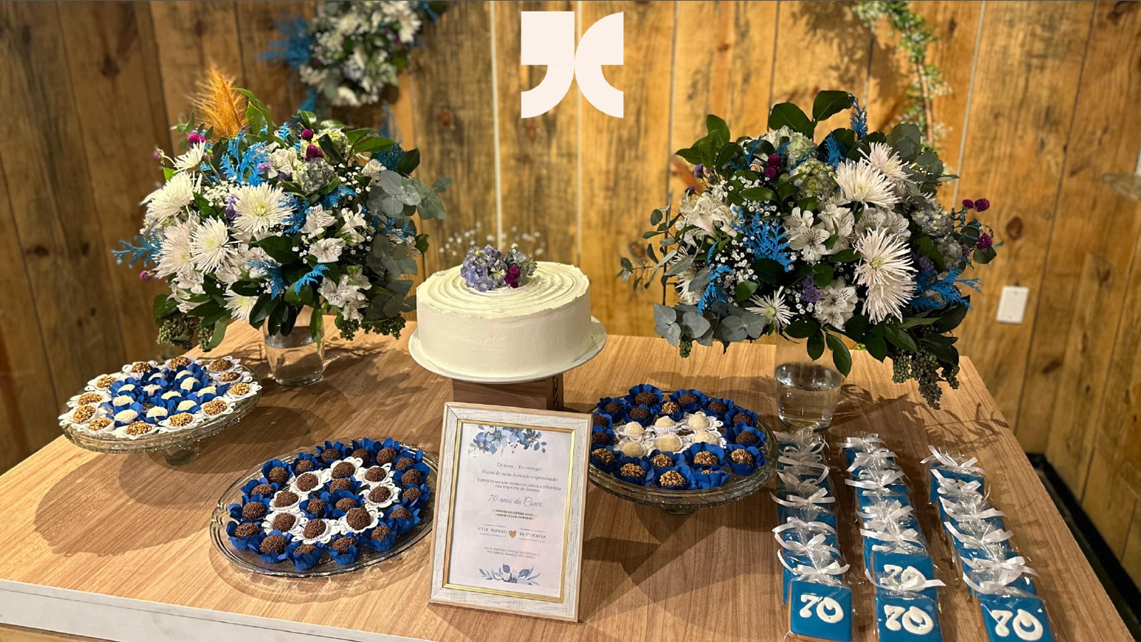 Mesa de comemoração com bolo, docinhos e arranjos florais